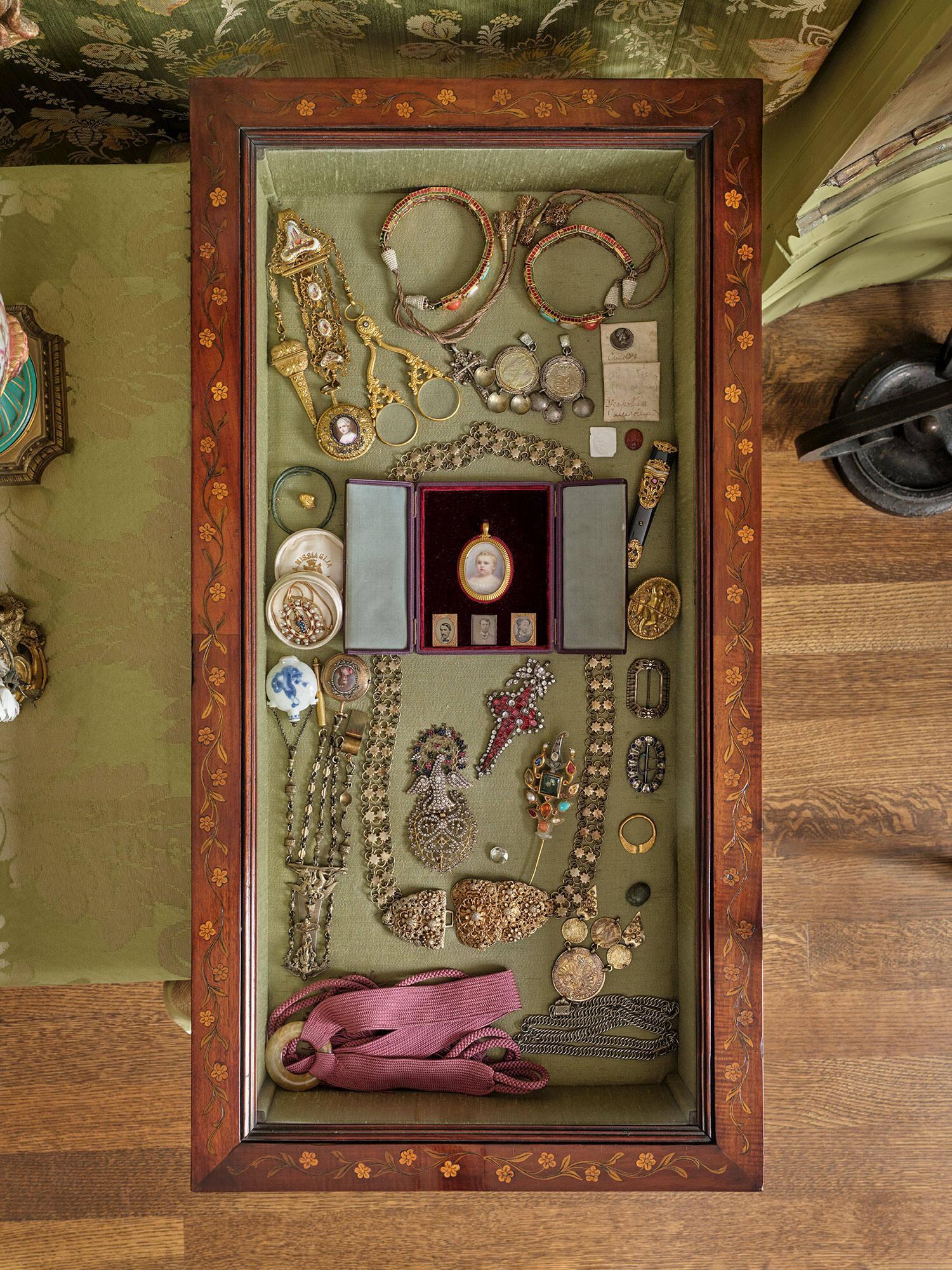 A glass display case with a variety of object including, in the center an open leather case containing miniature portraits of a light skinned infant boy, Jackie Gardner, a young white man with a mustache, Jack Gardner, a young white man, Joseph Peabody Gardner, and a young white woman, Isabella Gardner. 