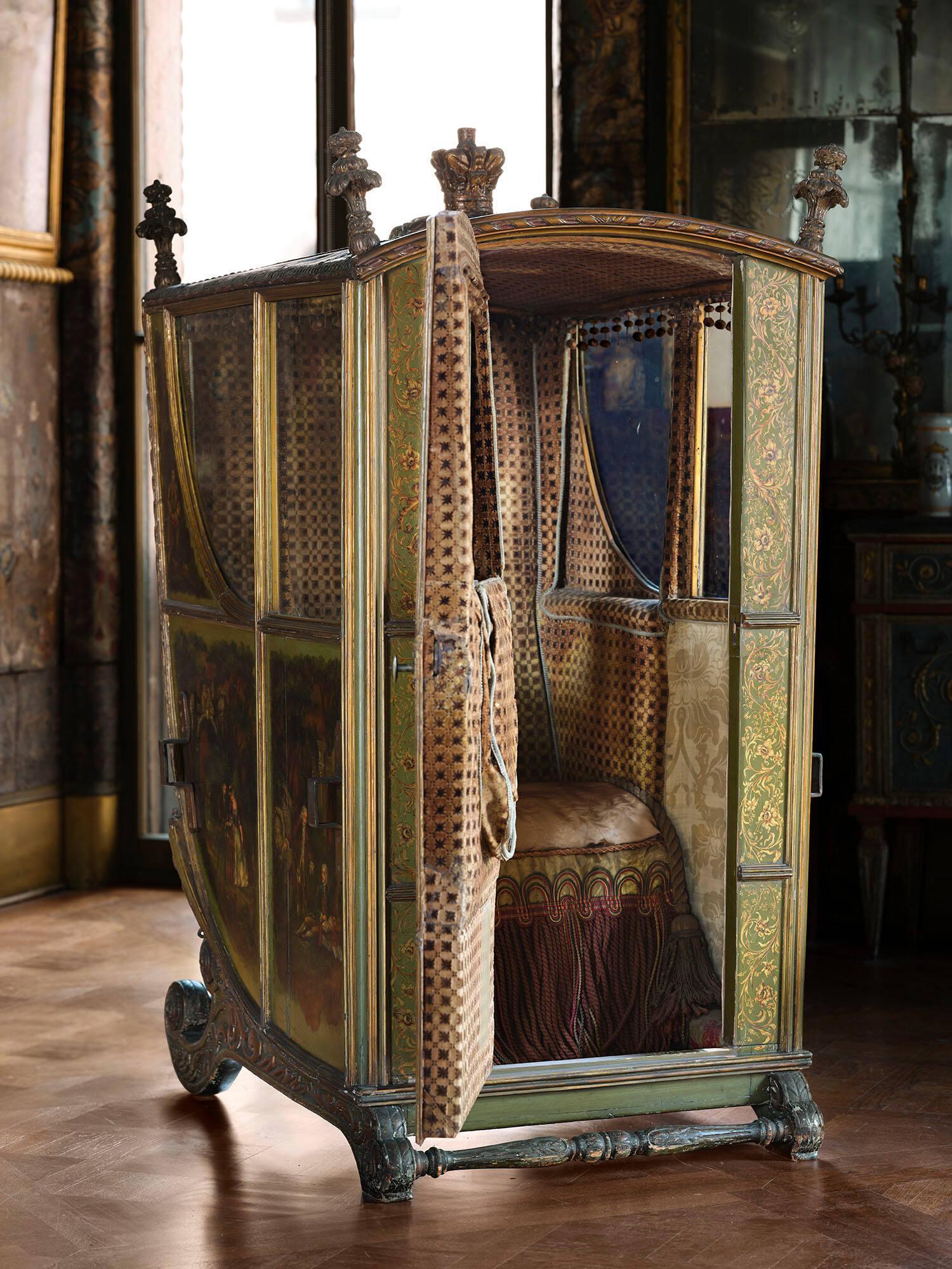 The sedan chair in the Gardner Museum’s Veronese Room with the door opened to show the interior lined with fabric and the cushion edged with long tassels