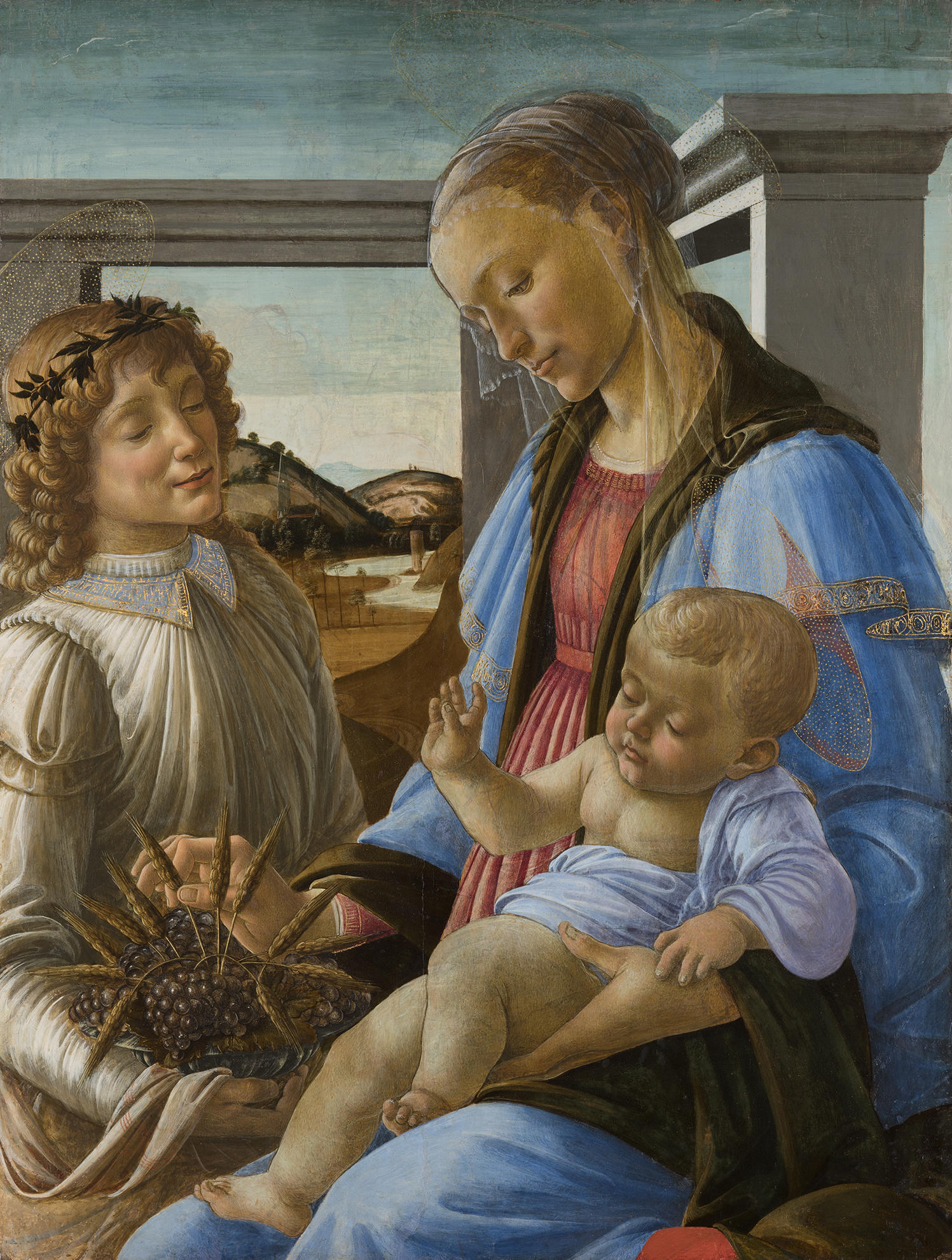 Boticelli’s painting Virgin and Child with an angel after the 2023 conservation treatment. A woman, the Virgin Mary, with a halo, veil, and wearing a blue robe holding an infant, the baby Jesus, in her lap. Standing to her left is a man, an angel, with a halo and wearing a white robe. He holds a pomegranate with sprigs of wheat. Behind them are white columns and a landscape.