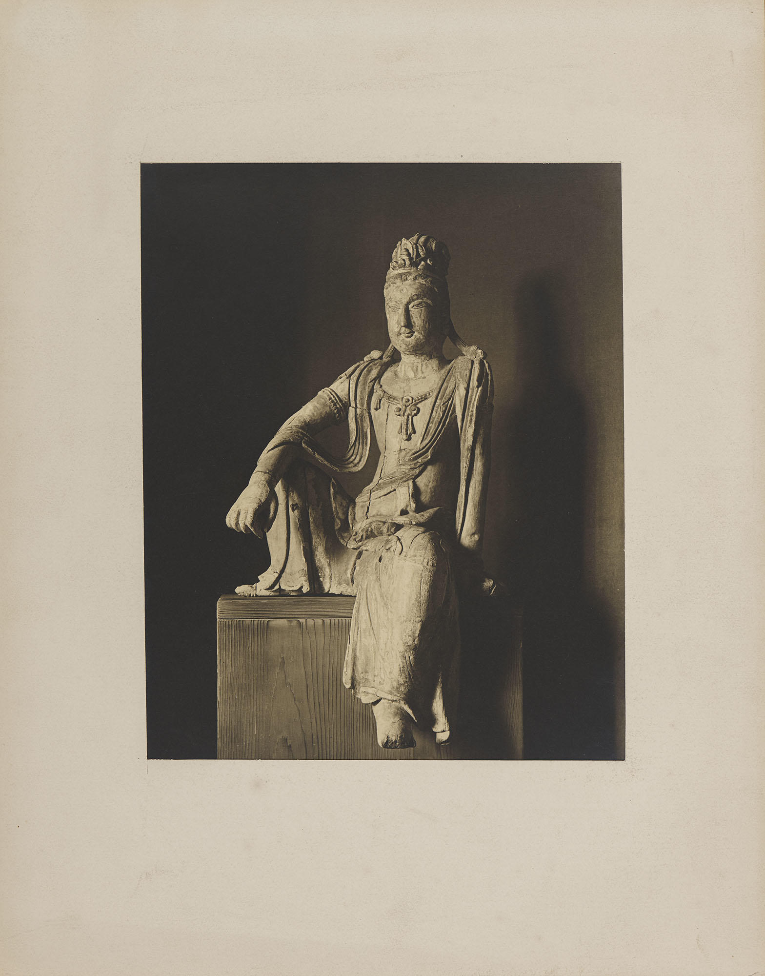 Black and white studio photograph of Guanyin sculpture sitting in the pose of Royal Ease,  mounted to board.
