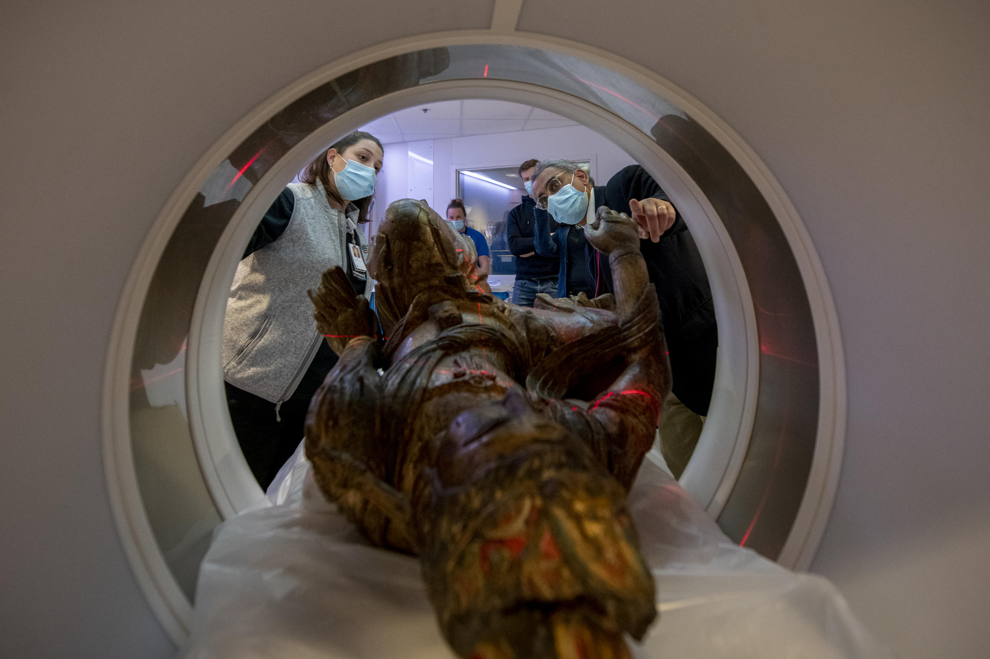 The Guanyin sculpture lays on the CT scanning bed inside the machine while medical staff tests the positioning with a laser alignment system.  