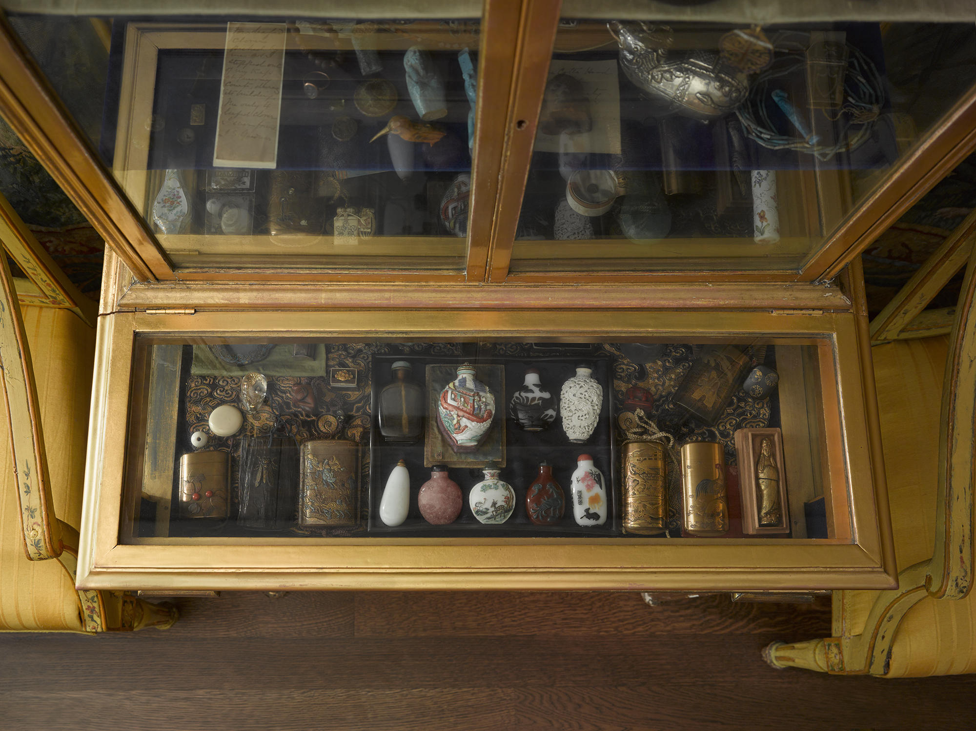 A shelf in a historic gilded, glass-door, cabinet with snuff bottles in the Little Salon of the Gardner Museum.