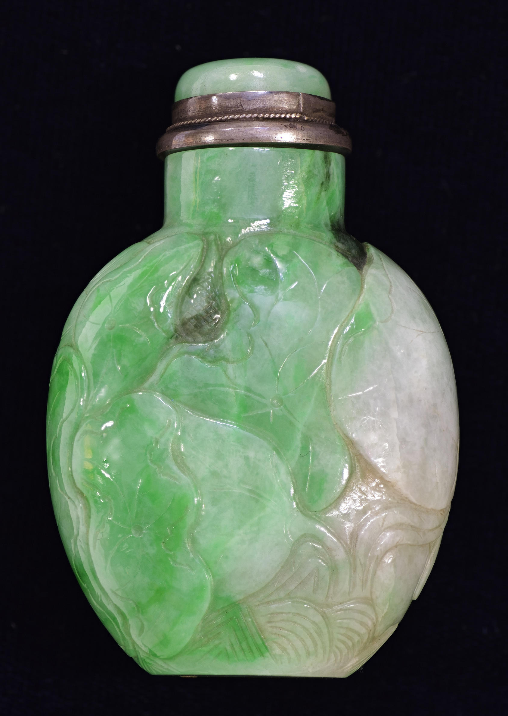 A green and white oval-shaped snuff bottle and stopper. There are nature motifs and patterns carved into the surface.