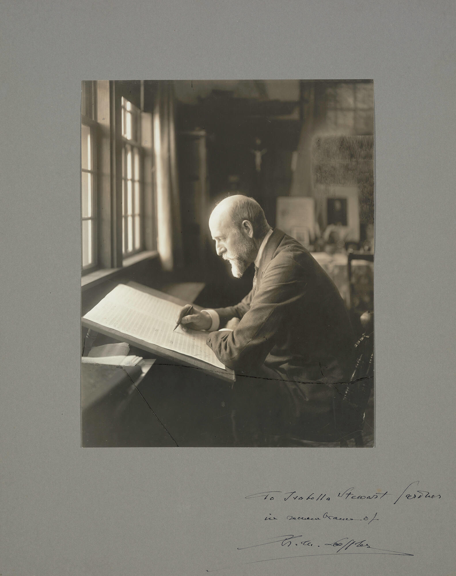 A black and white photograph of a white man, Charles Martin Loeffler, seated at a desk working on a musical score.