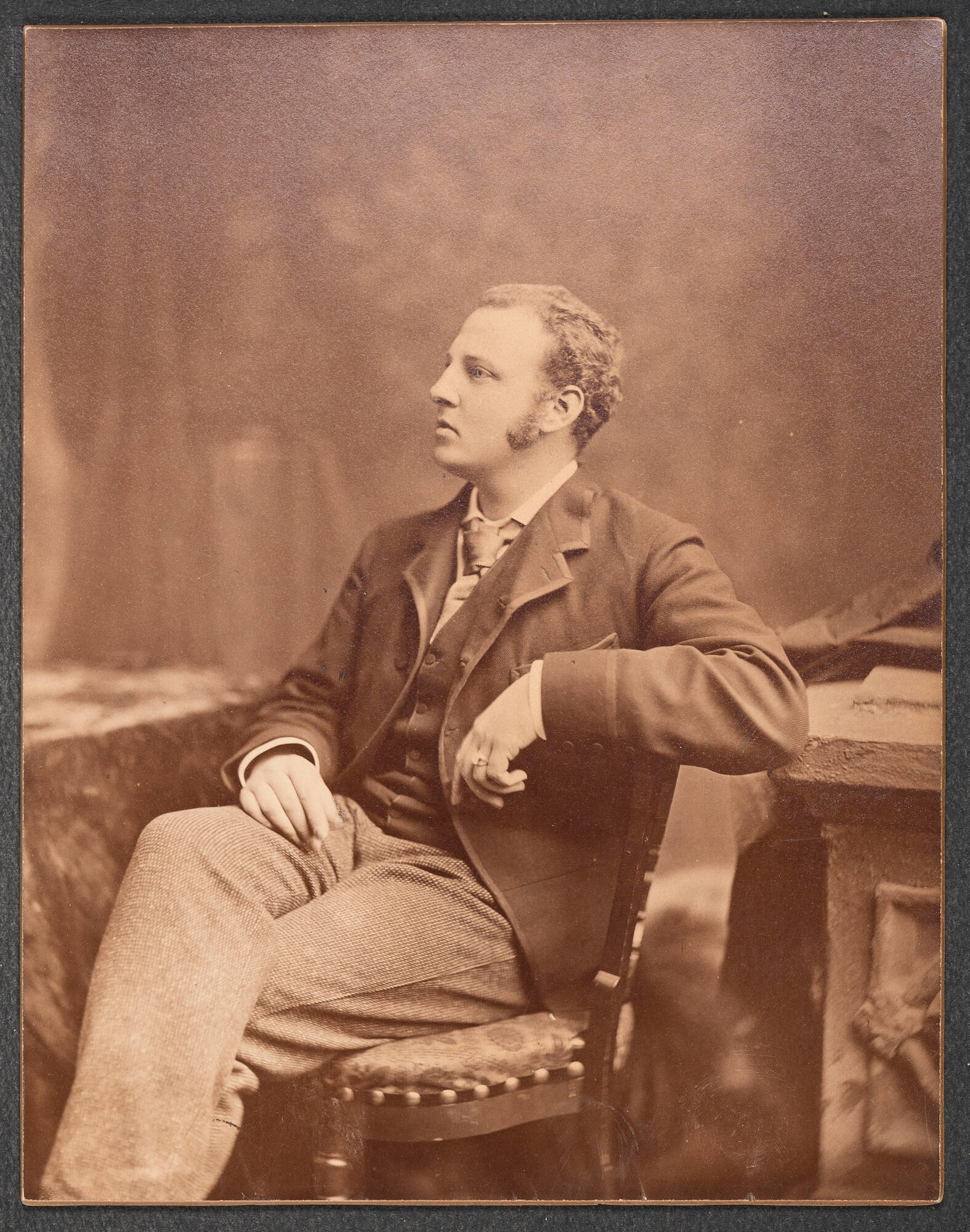A sepia toned photograph of a man,  F. Marion Crawford, with light skin and curly hair seated in a chair.