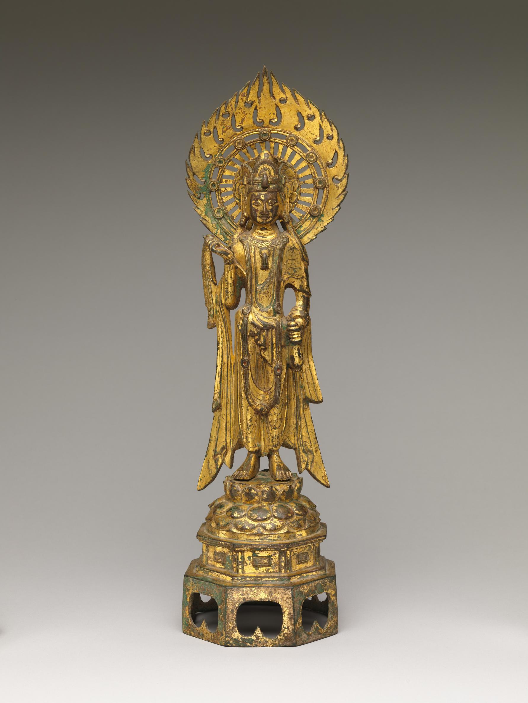 A gold statuette of the standing figure of Guanyin with a flaming circle behind their head.