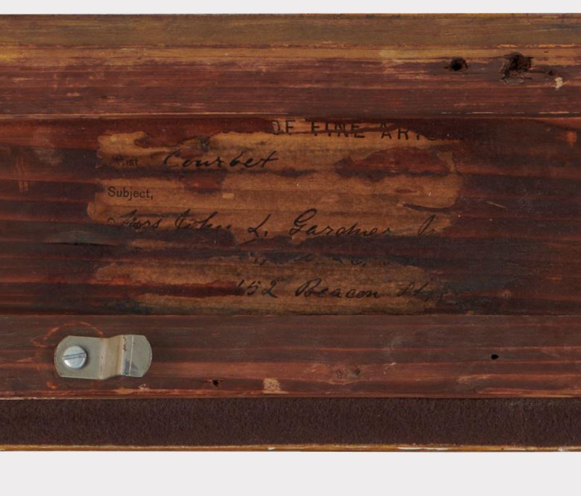 A photograph of a torn label from a Gustave Courbet painting that has handwriting in ink that is adhered to a wood frame. 