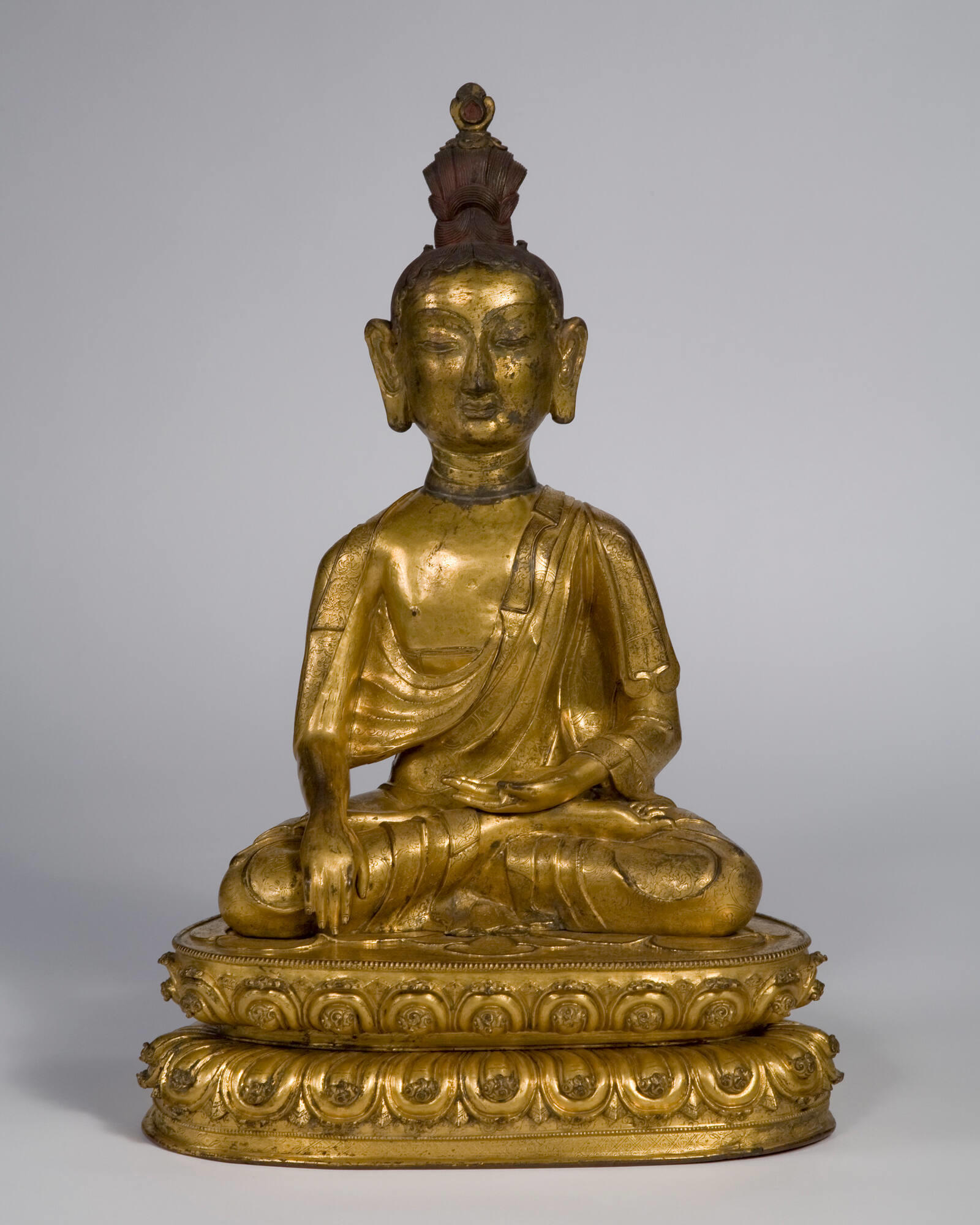 Gold statue of the Buddha sits cross-legged with his hands resting on his knee and lap. 