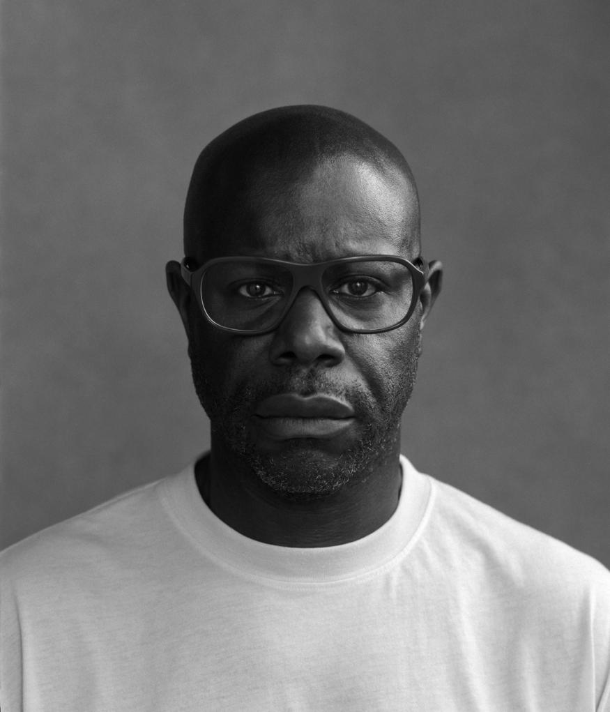 Black and white photo of Steve McQueen, an African American man with a white t-shirt against a grey background. 