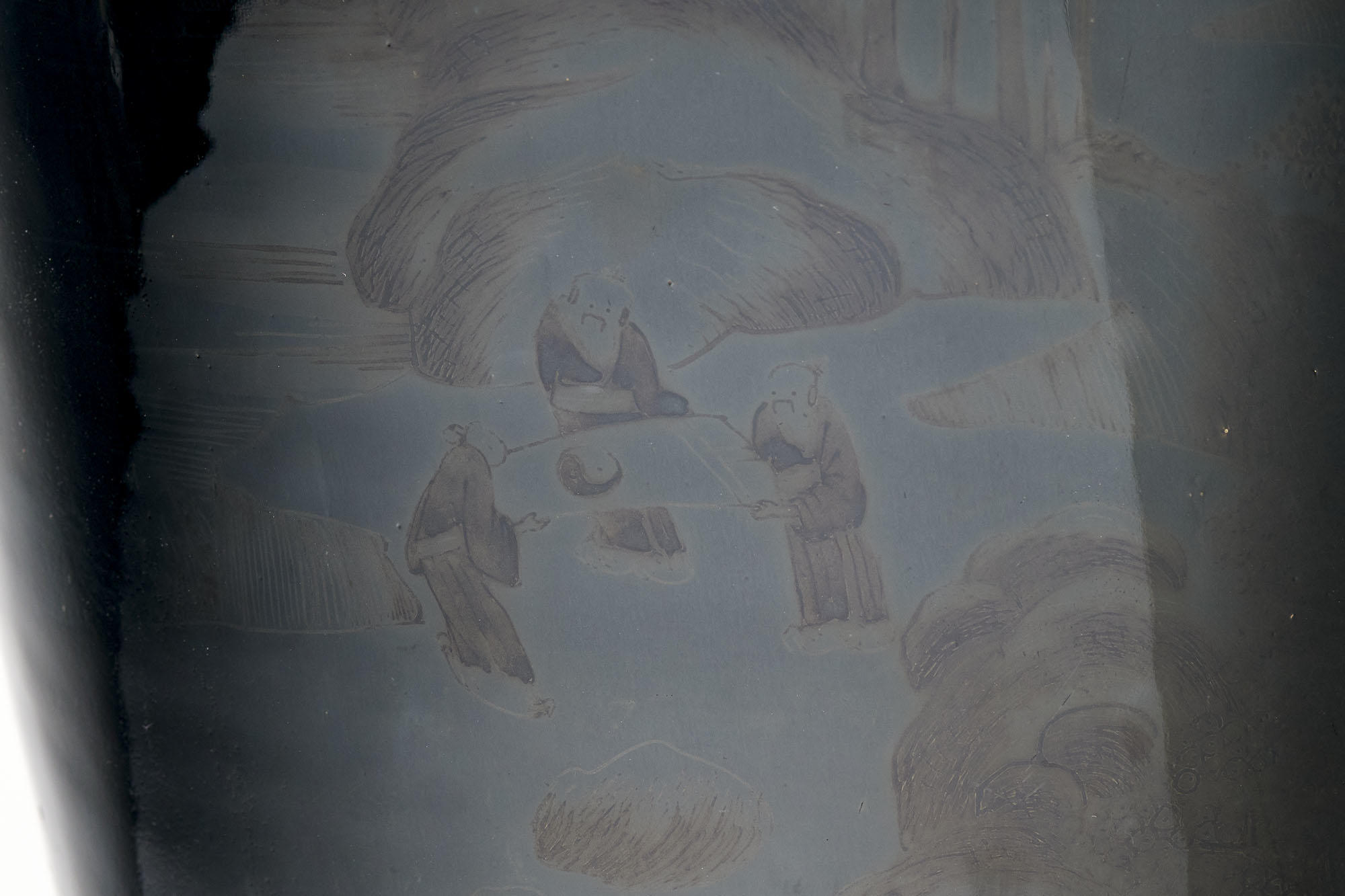 Detail of trace decoration showing three male figures in robes standing outside surrounded by textured rocks. Two hold a scroll bearing the yin and yang symbol. The third figure looks down at the scroll.