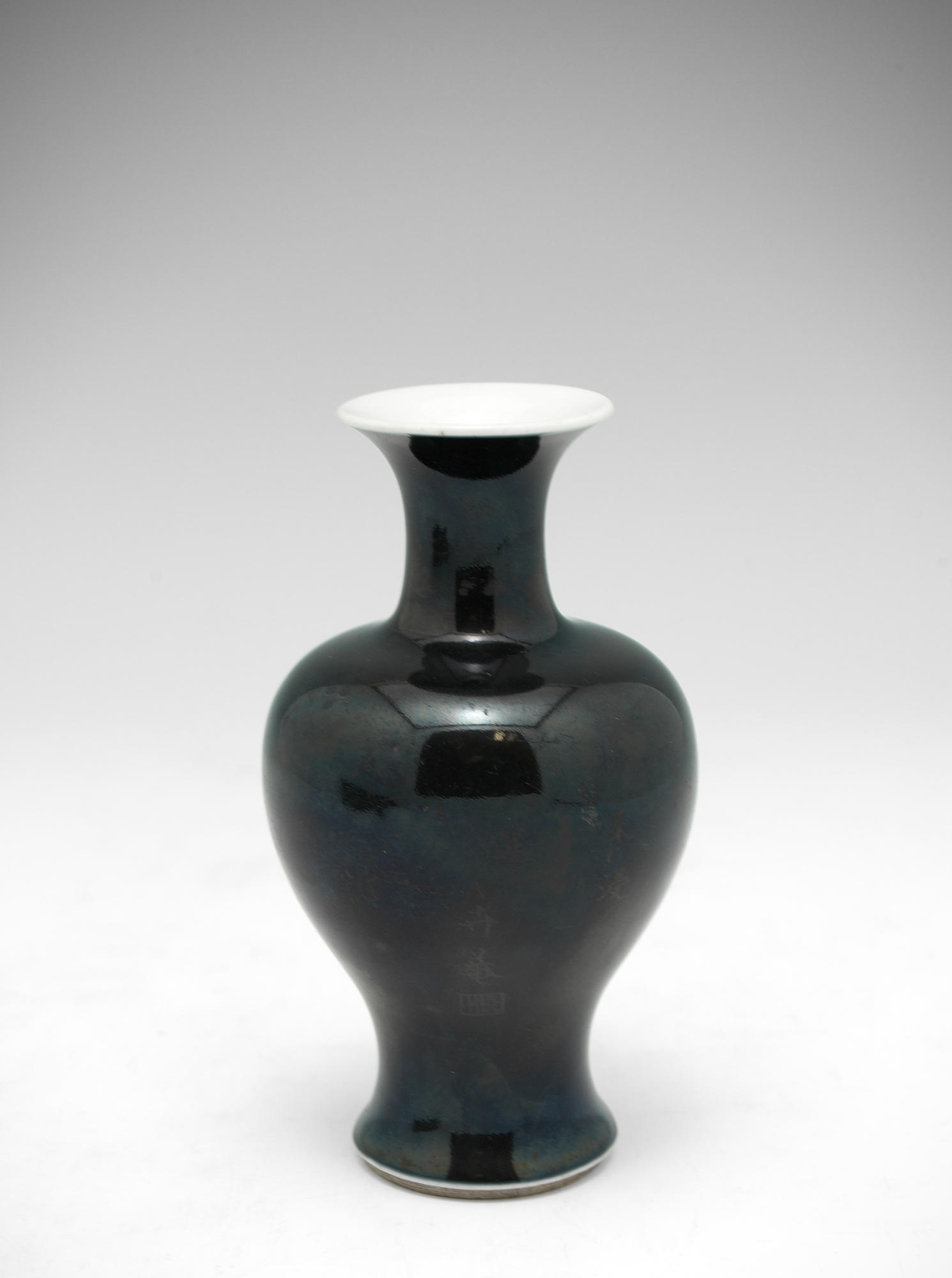 A black vase, taller than it is wide, with a rim that turns outward, a short neck, and a broad shoulder that curves to a narrow base with traces of gold characters. 
