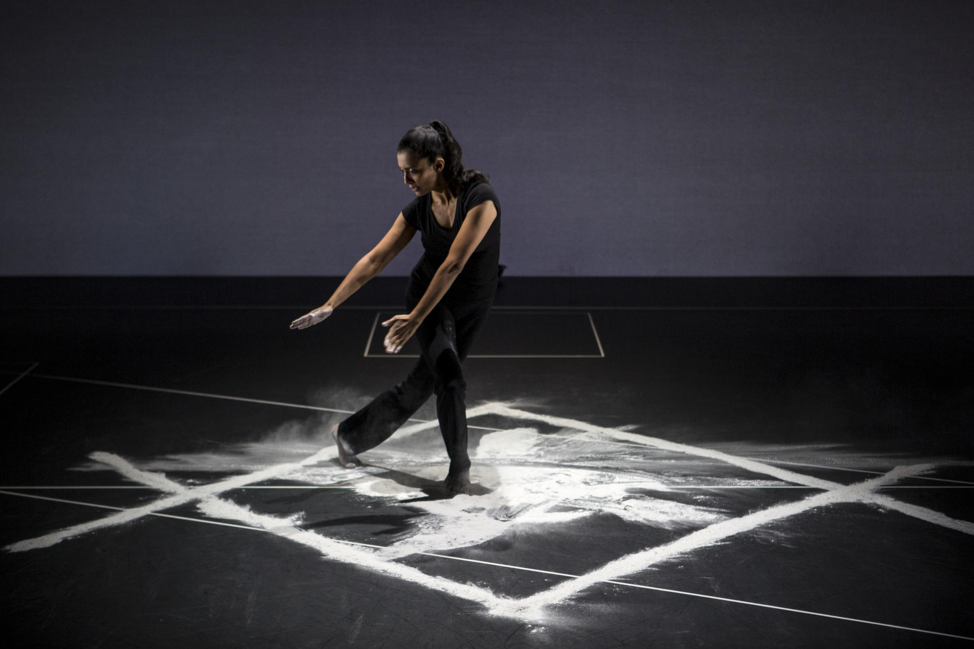 Woman with long dark hair dancing on a white image on a black stage. 