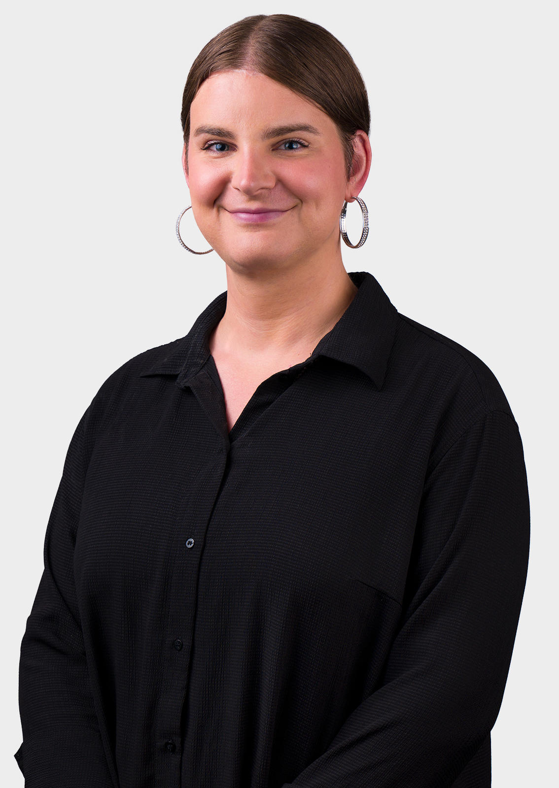 Woman with a black, button top, brown hair parted in the middle and pulled back wearing large hoop earirings. 