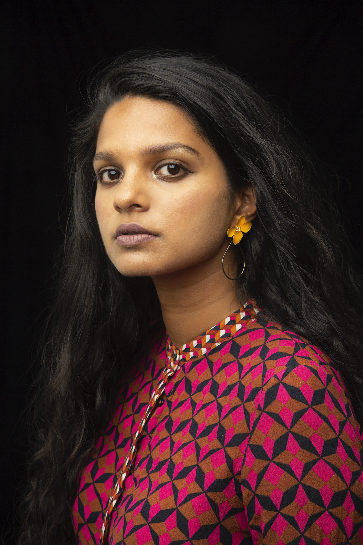 Young woman with long dark hair in red dress with black and gold lines looking at the camera