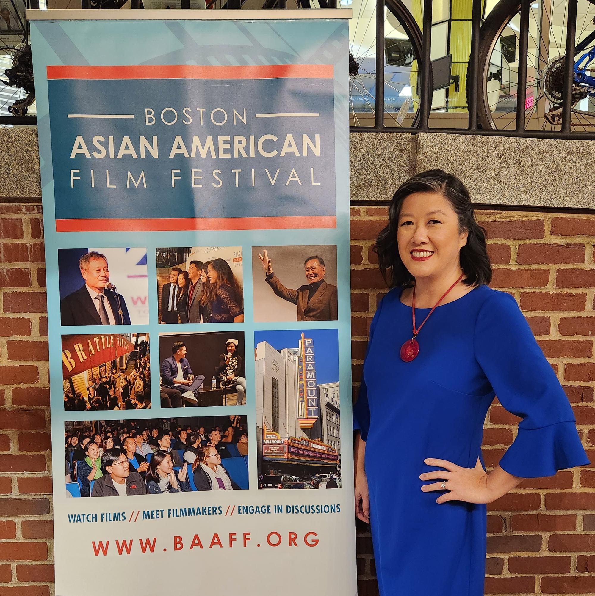 Asian woman in a blue dress standing next to a sign for the Boston Asian American Film Festival