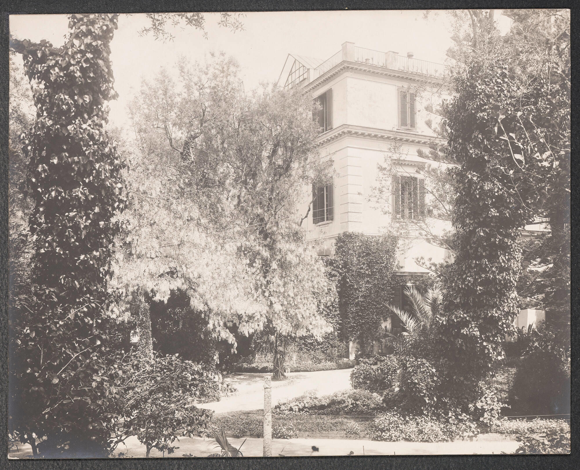 Black and white photograph of a three story white building in a lush Italian landscape.