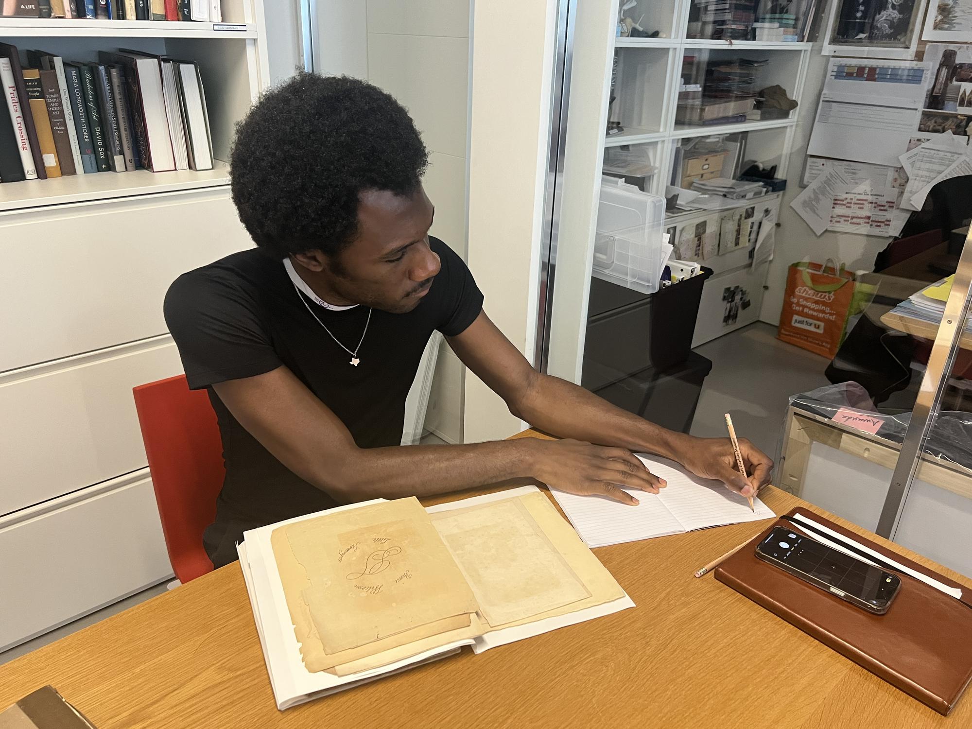 Man in black shirt taking notes with a book in front of him 