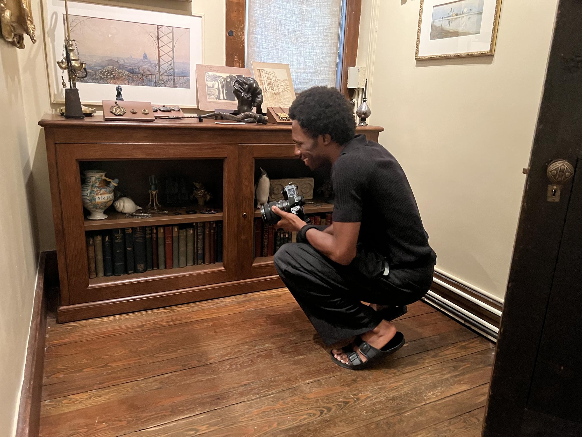 Man in black shirt and pants, crouching down to look at items in a waist-high shelf with glass dorrs 