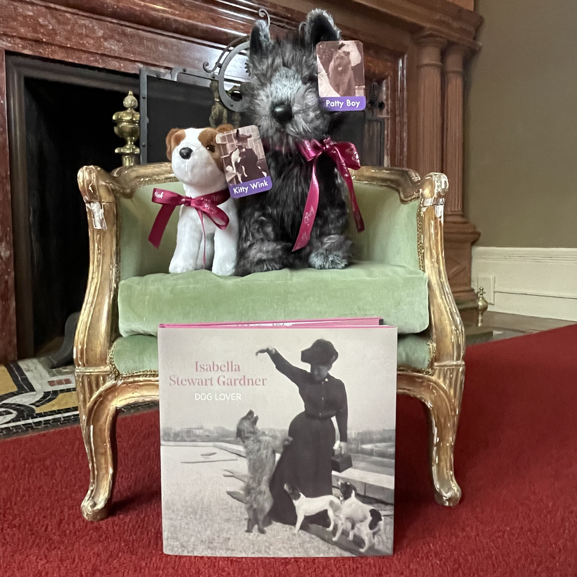 Two plush dogs on a decorative sheet with a copy of the book Isabella Stewart Gardner, Dog Lover 