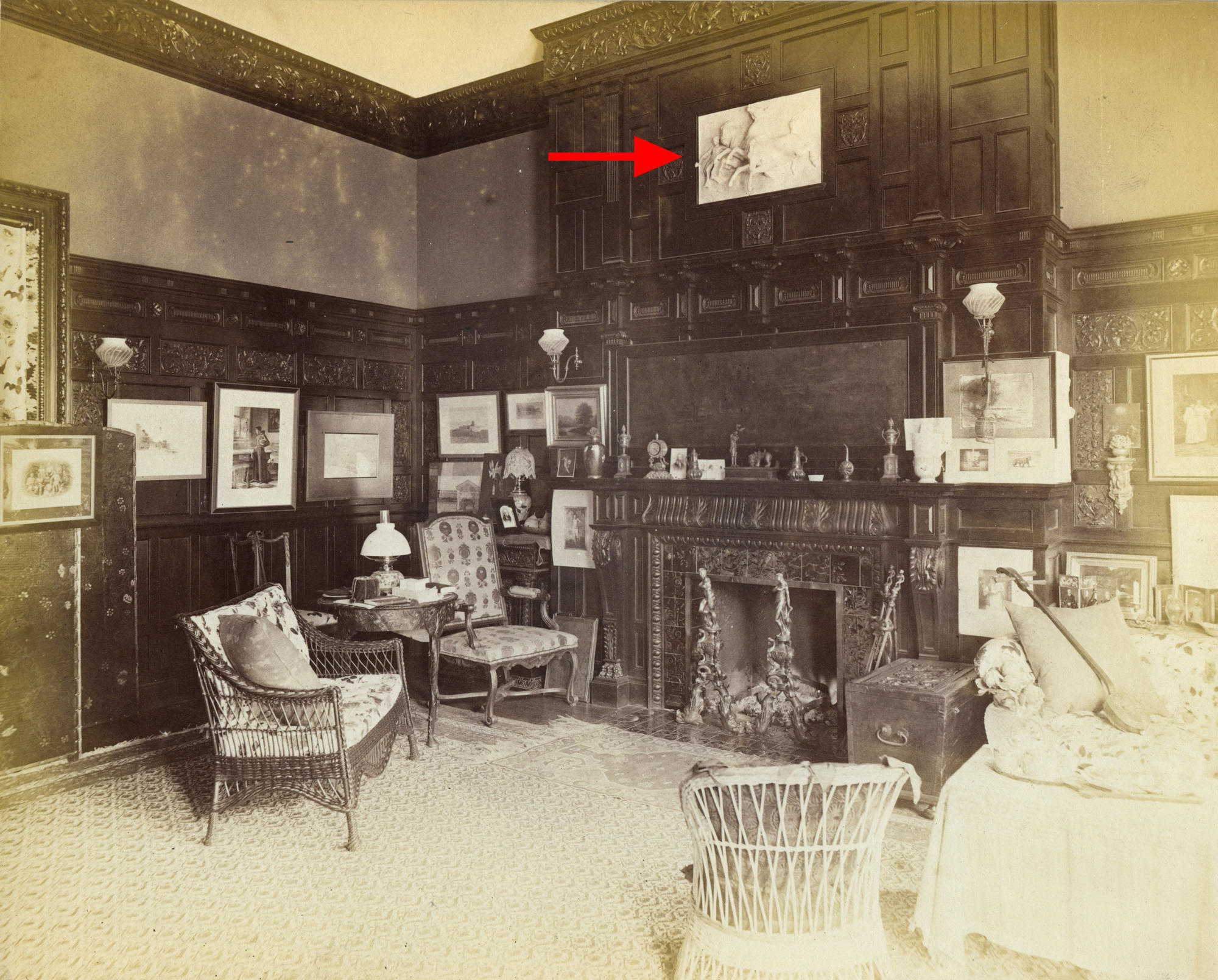 A black and white photograph of a dark wood paneled room, with a red arrow indicating William Morris Hunt’s plaster cast of horses over the mantel