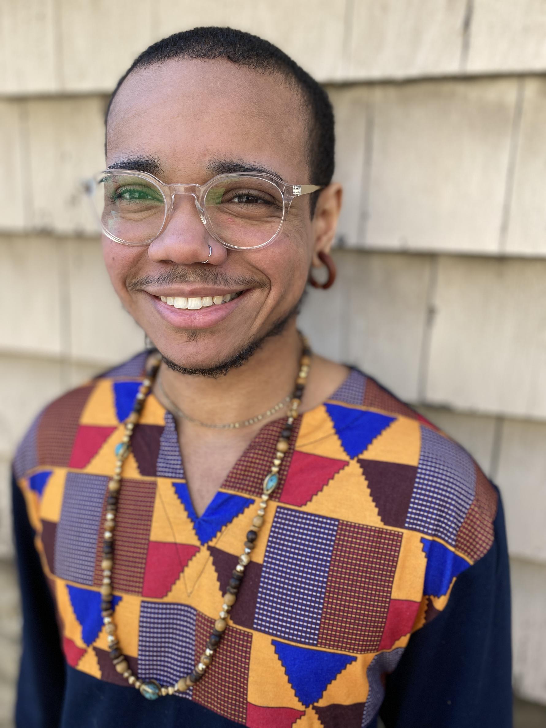 Young man with short,cropped hair, glasses with a big smile and multi colored shirt. 