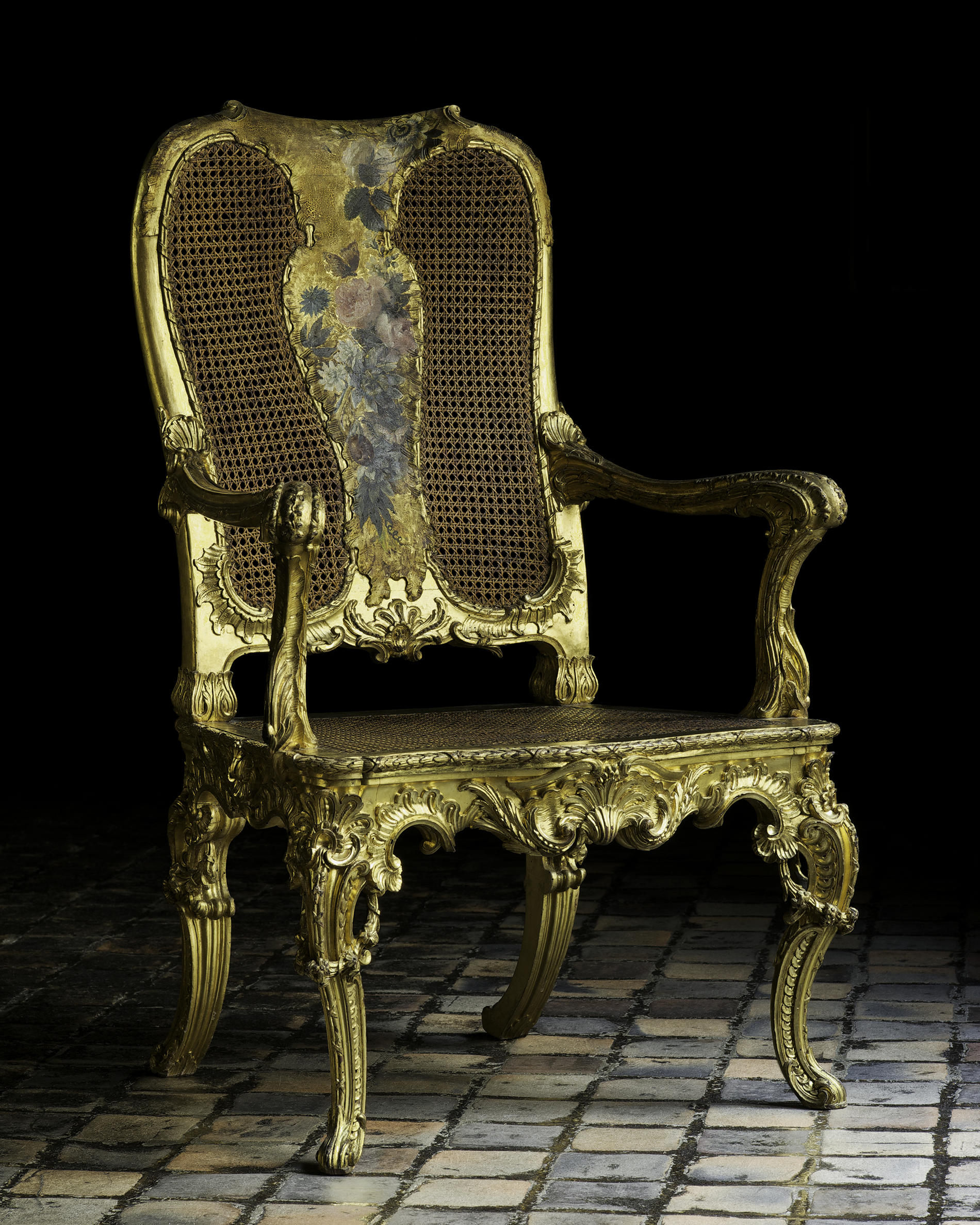 A color photograph of one of the giltwood armchairs with a shadowed background.