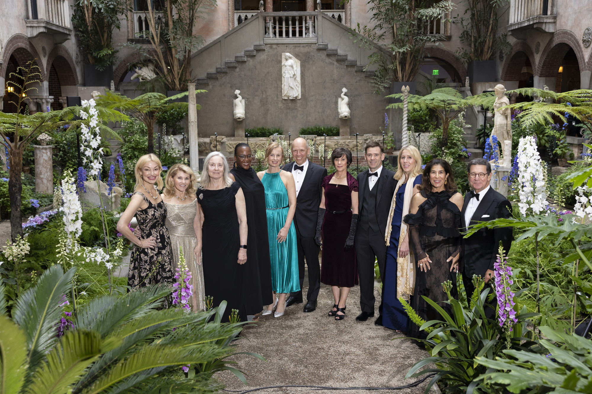 A group of men and women in gowns and tuxedos lined up in the middle of the court yard. 