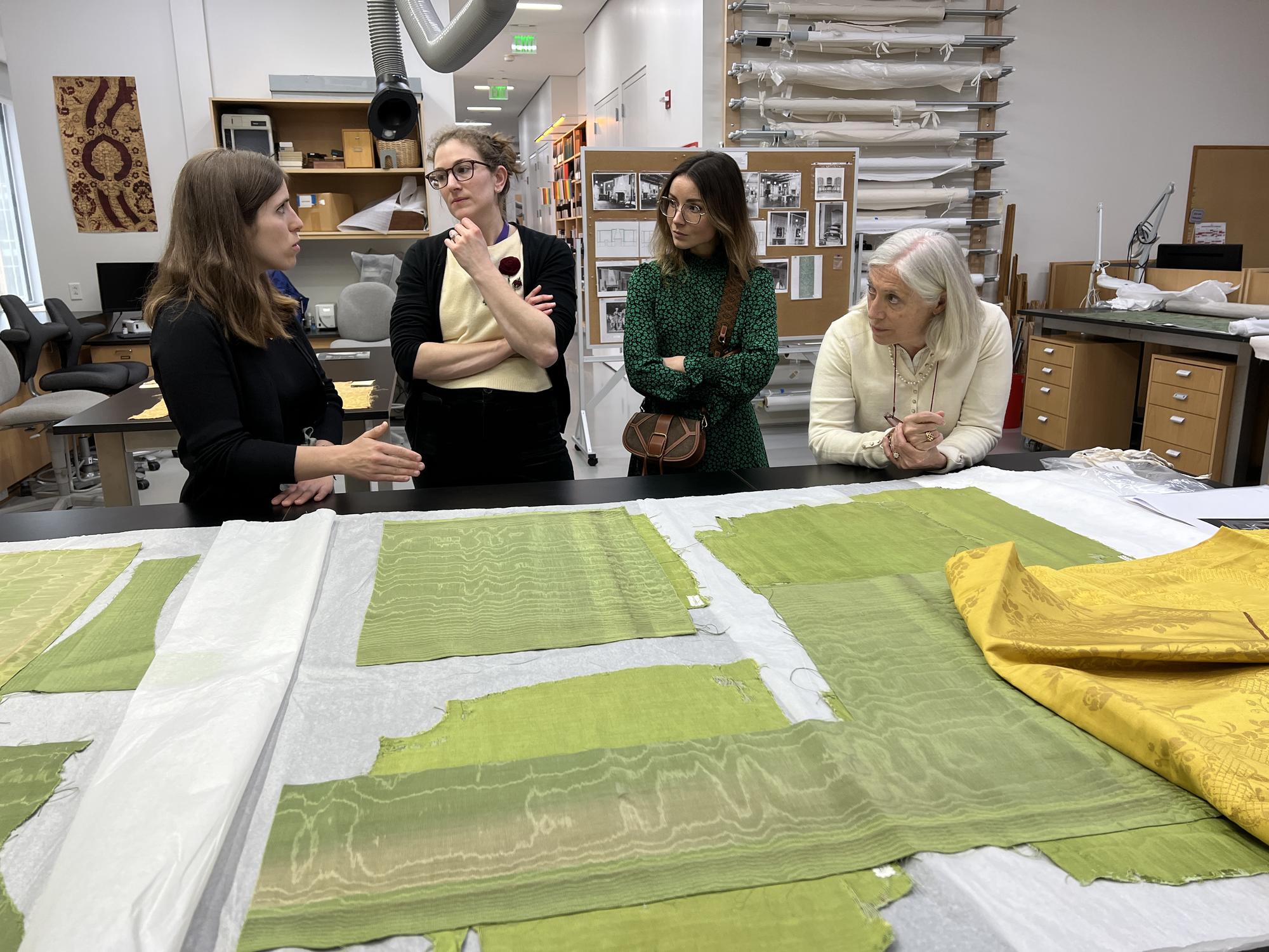 Four women in front of a large counter with pieces of decorative green material laid out