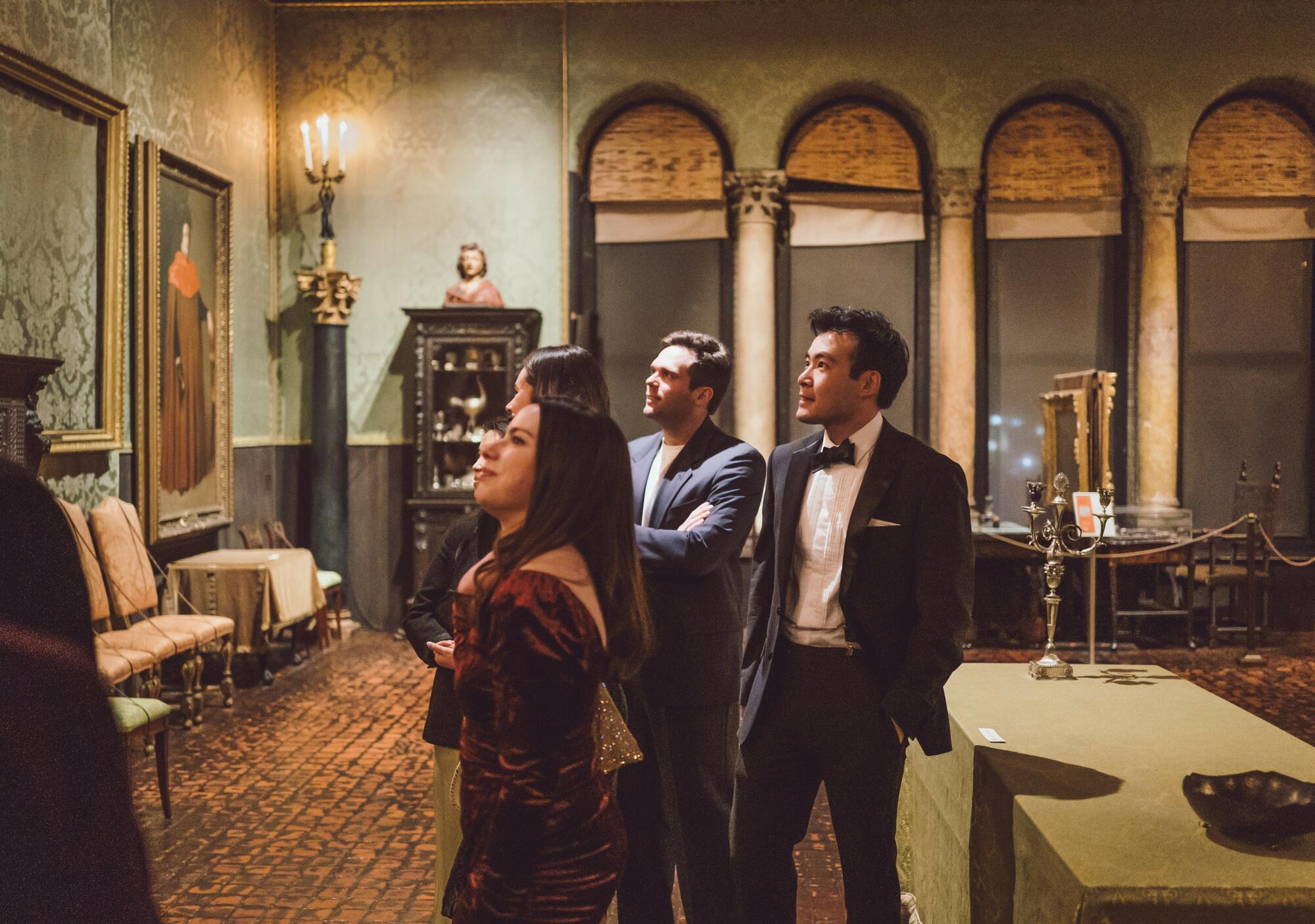 Two men and women dressed in formal attire looking at art. 