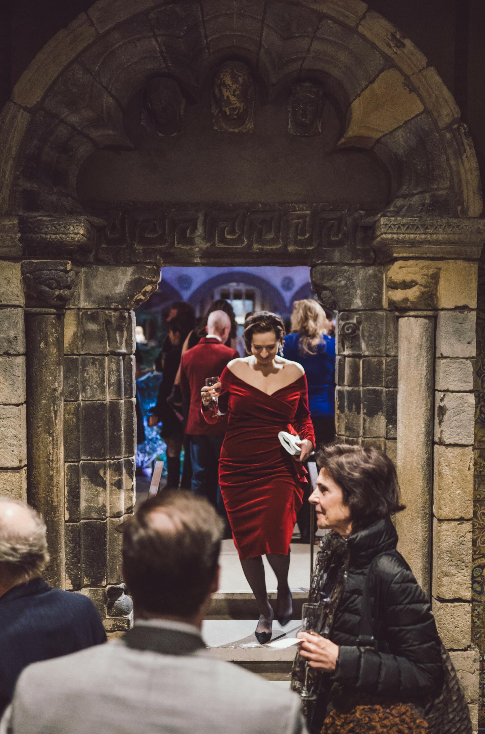 Woman in a red velvet dress walking through one of the arches from the courtyard