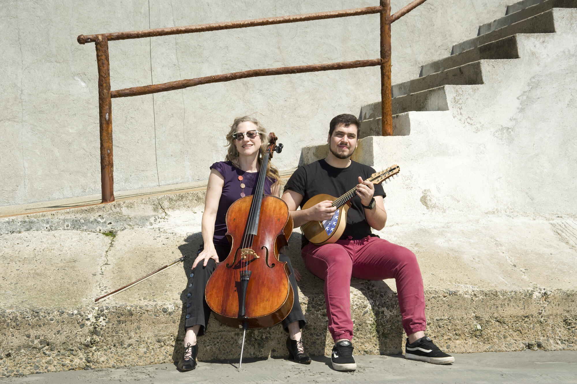 Photo of a man and woman sitting outside holding string instruments