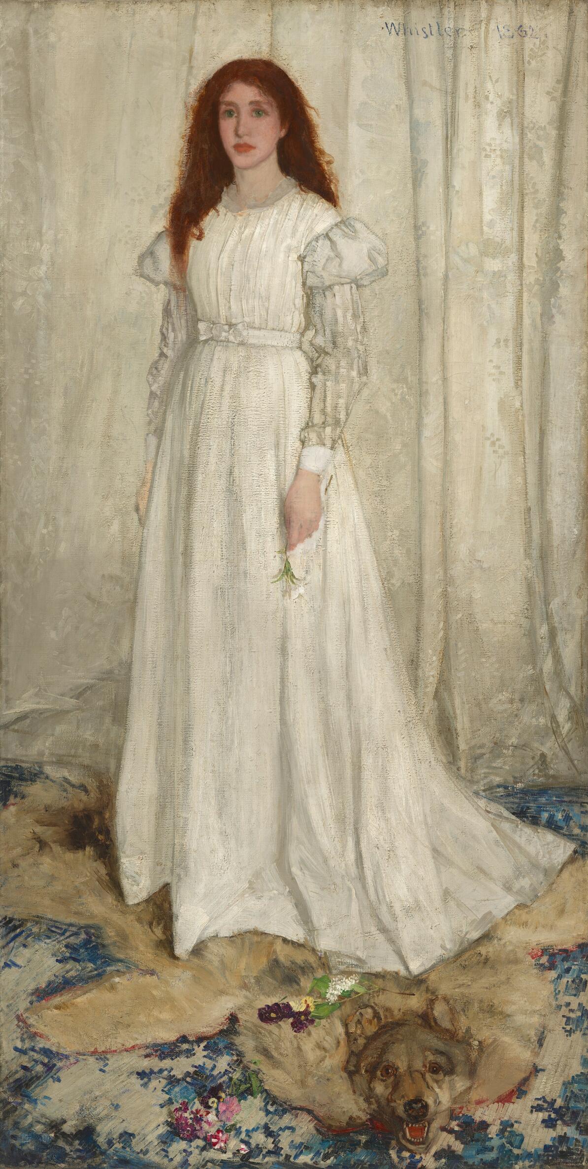 A young white woman wearing a long, flowing white dress, stands in front of a white curtain in this vertical portrait painting. She holds a white lily by her side in her left hand, while yellow and purple flowers lie scattered on the animal pelt beneath her feet.