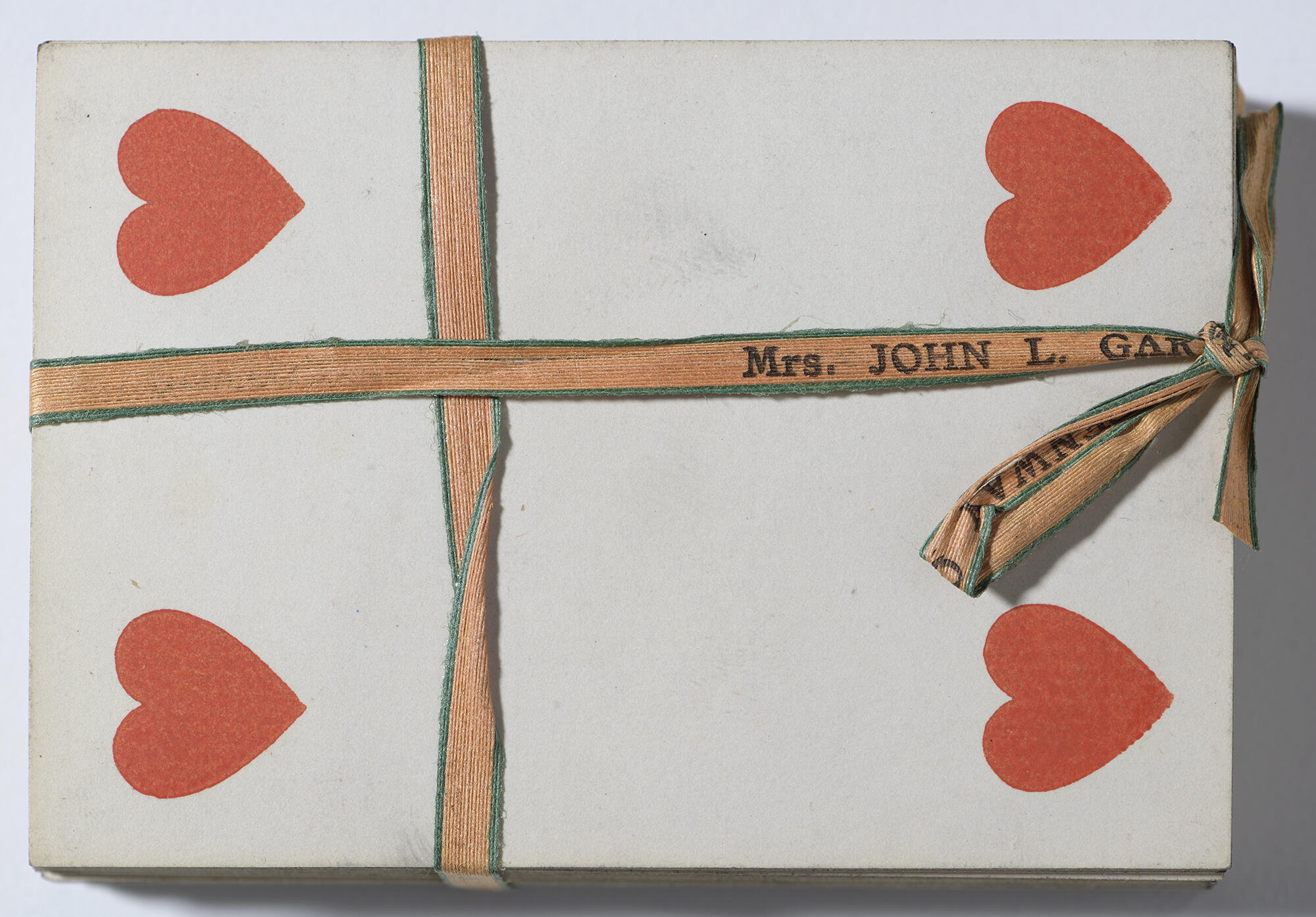 An overhead view of a deck of playing cards, with the four of hearts facing up, secured together by an orange ribbon that is personalized with Isabella’s name.
