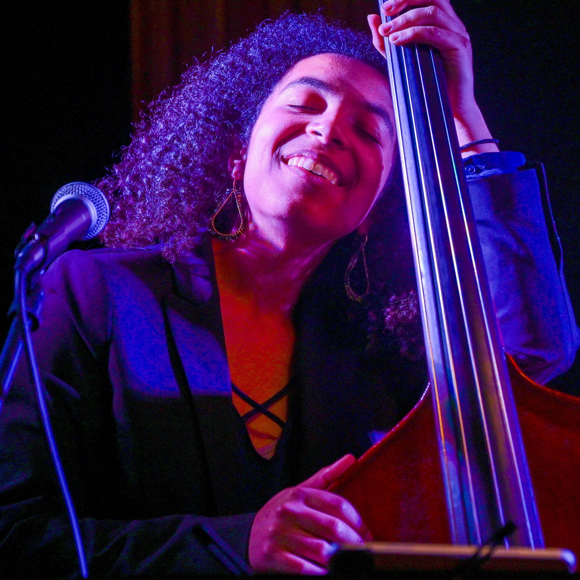 Woman with long, curly hair looking upwards, eyes closed holding a bass.  