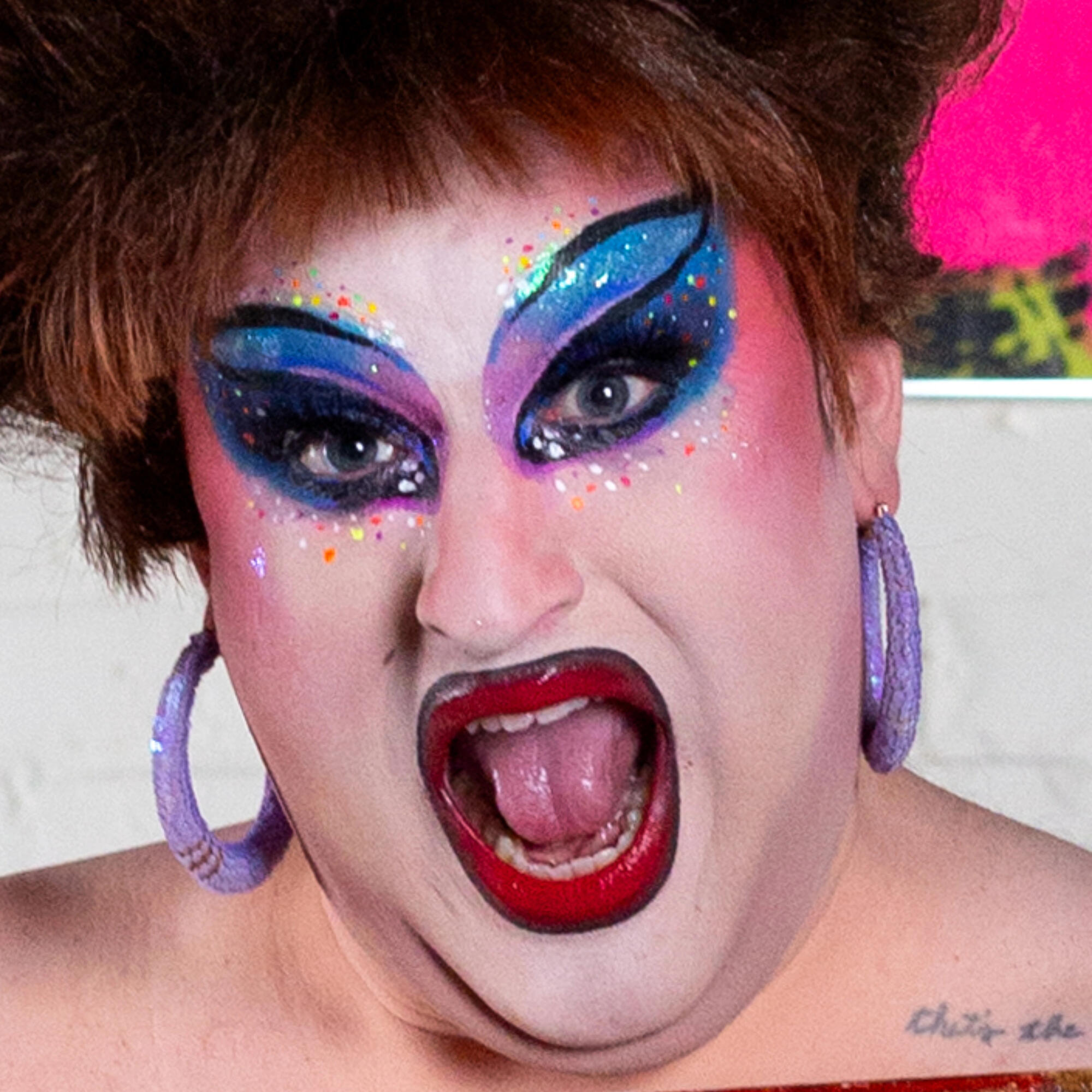 Person with short red hair and colorful, blue, sparkle eye makeup and bright red lipstick. 