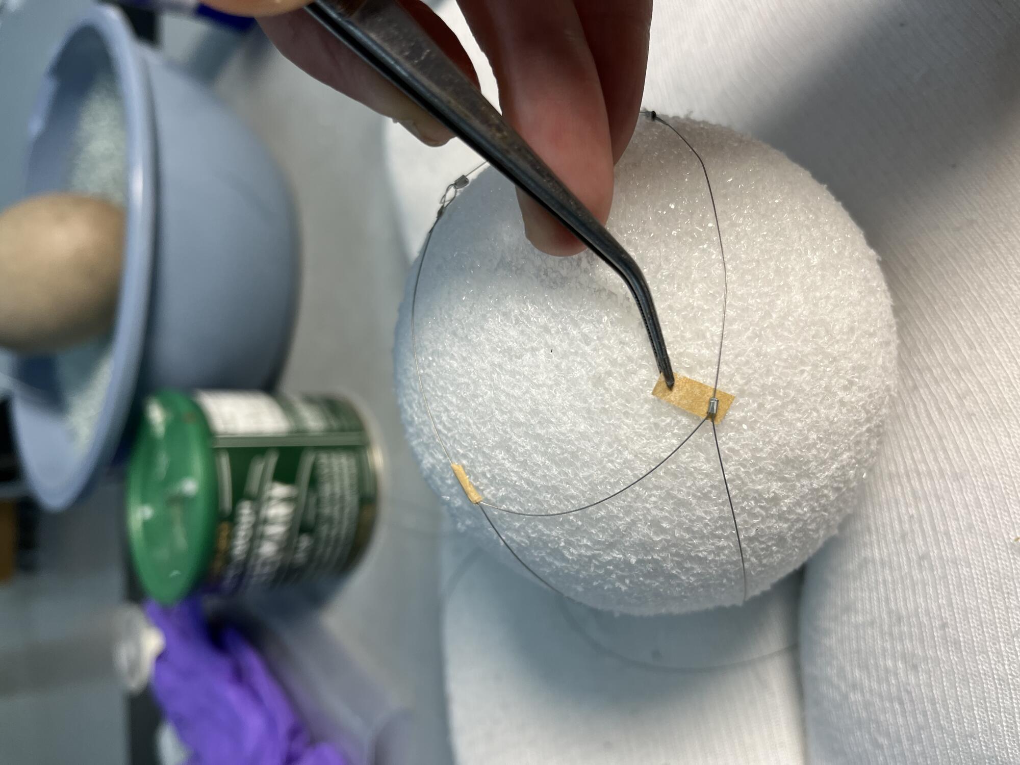 Detail of person using tweezers to apply toned Japanese tissue paper strips around metal crimps.     