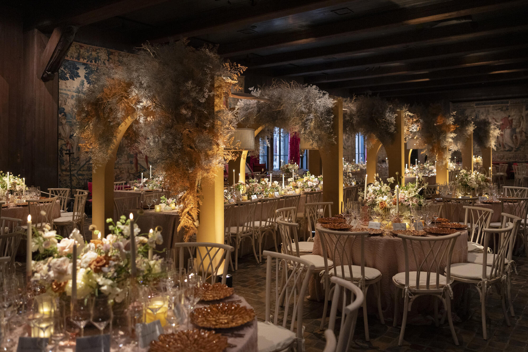 Elegant dining area with vaulted wood ceiling in shades of sand and yellow with wispy branches hanging from above. 