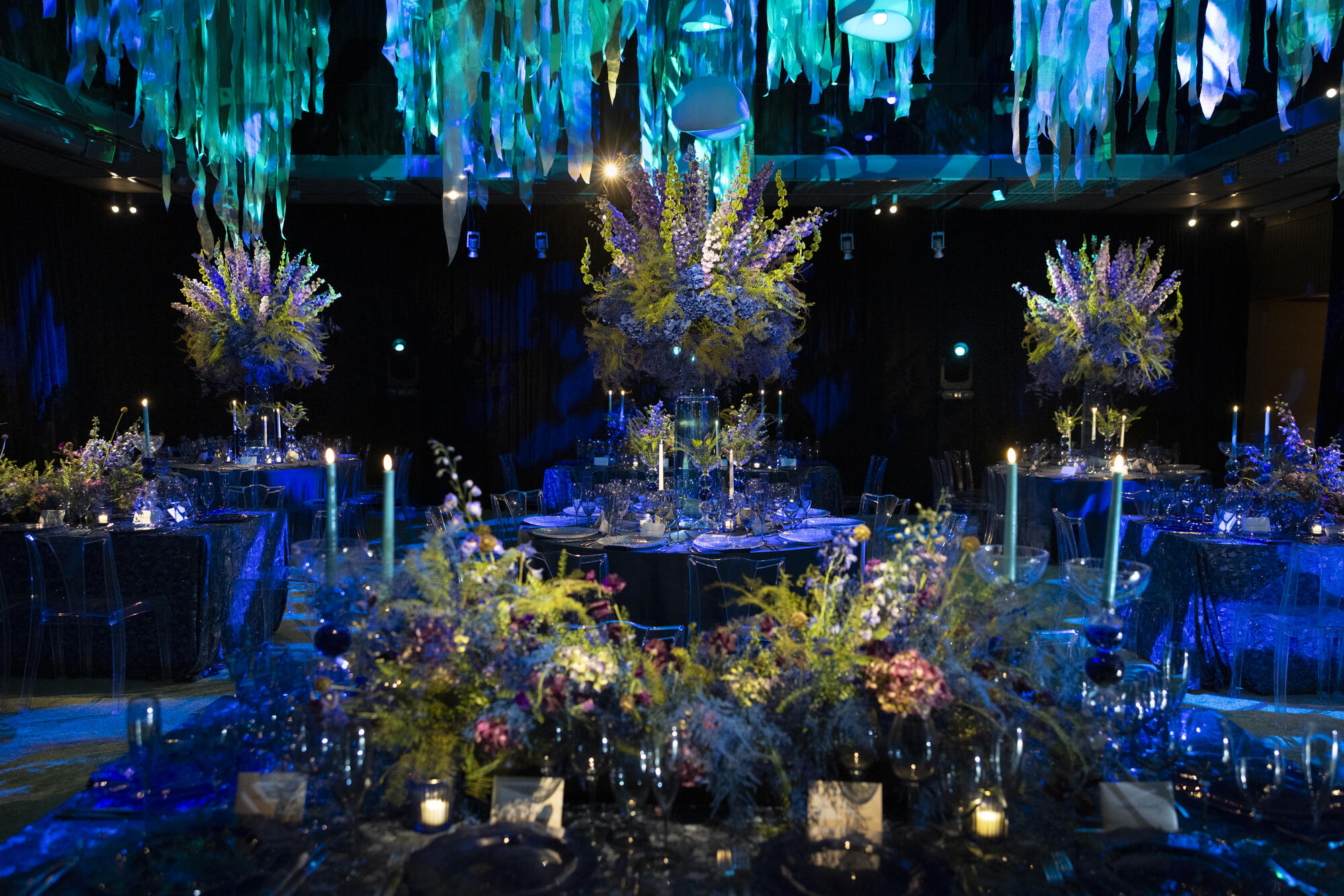 Elegent dining area that resembles an underwater scene with lots of blues, candles and elegant lighting hanging from the ceiling. 