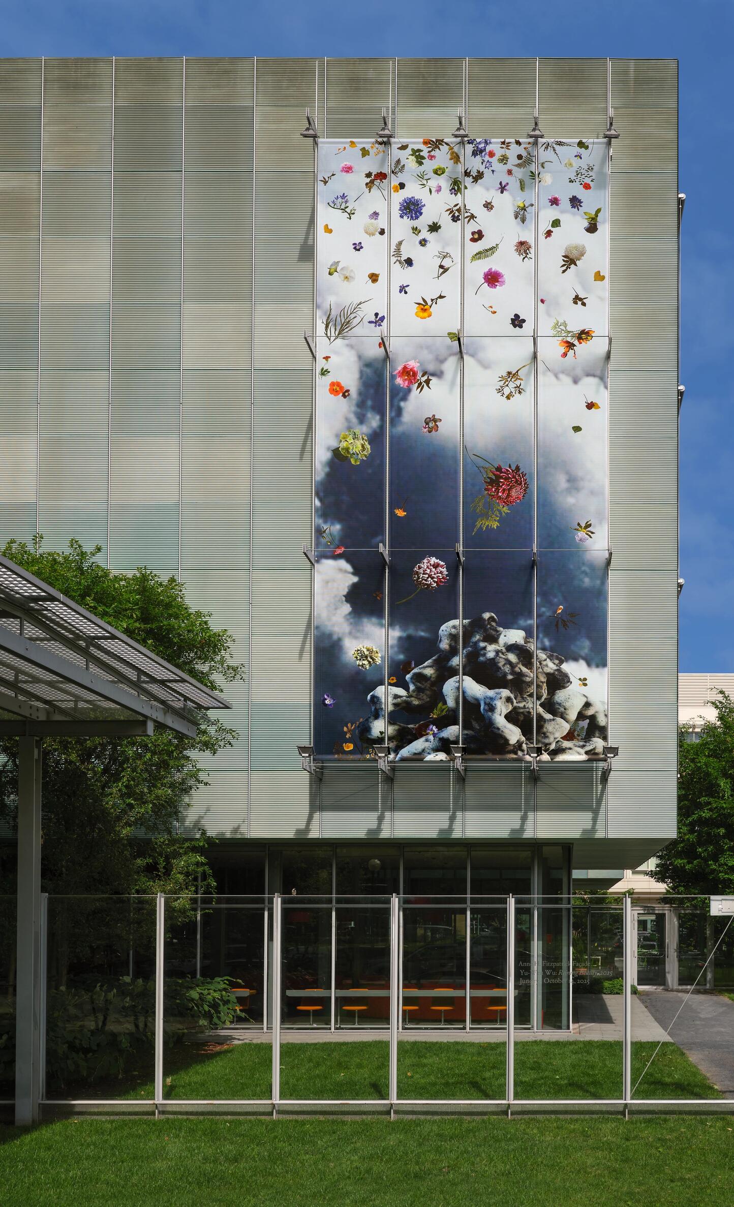 mage of a large image on the facade of the Museum with hundreds of flowers floating in the sky with clouds and a grey sky above a rocky mountain