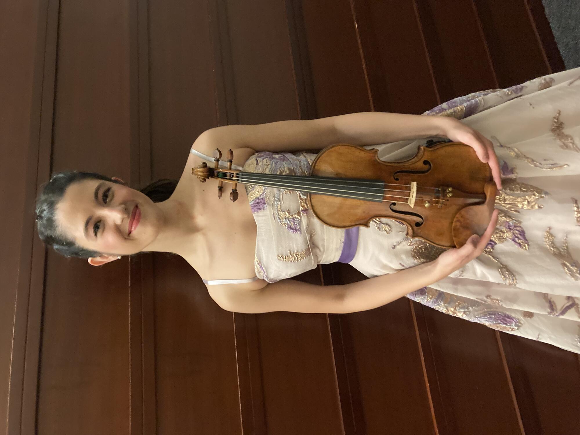 A photograph of a young white woman holding a violin.