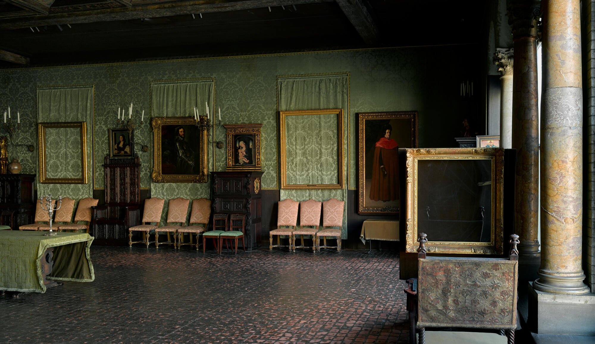 A room with European old-master paintings, sculpture, and furniture arranged eclectically. The lower half of the image shows a line of chairs, all upholstered in matching floral damask. 
