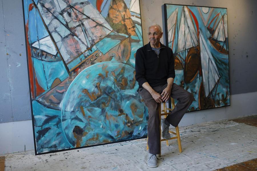 African American man with grey hair and glasses sitting in front of two large canvases 