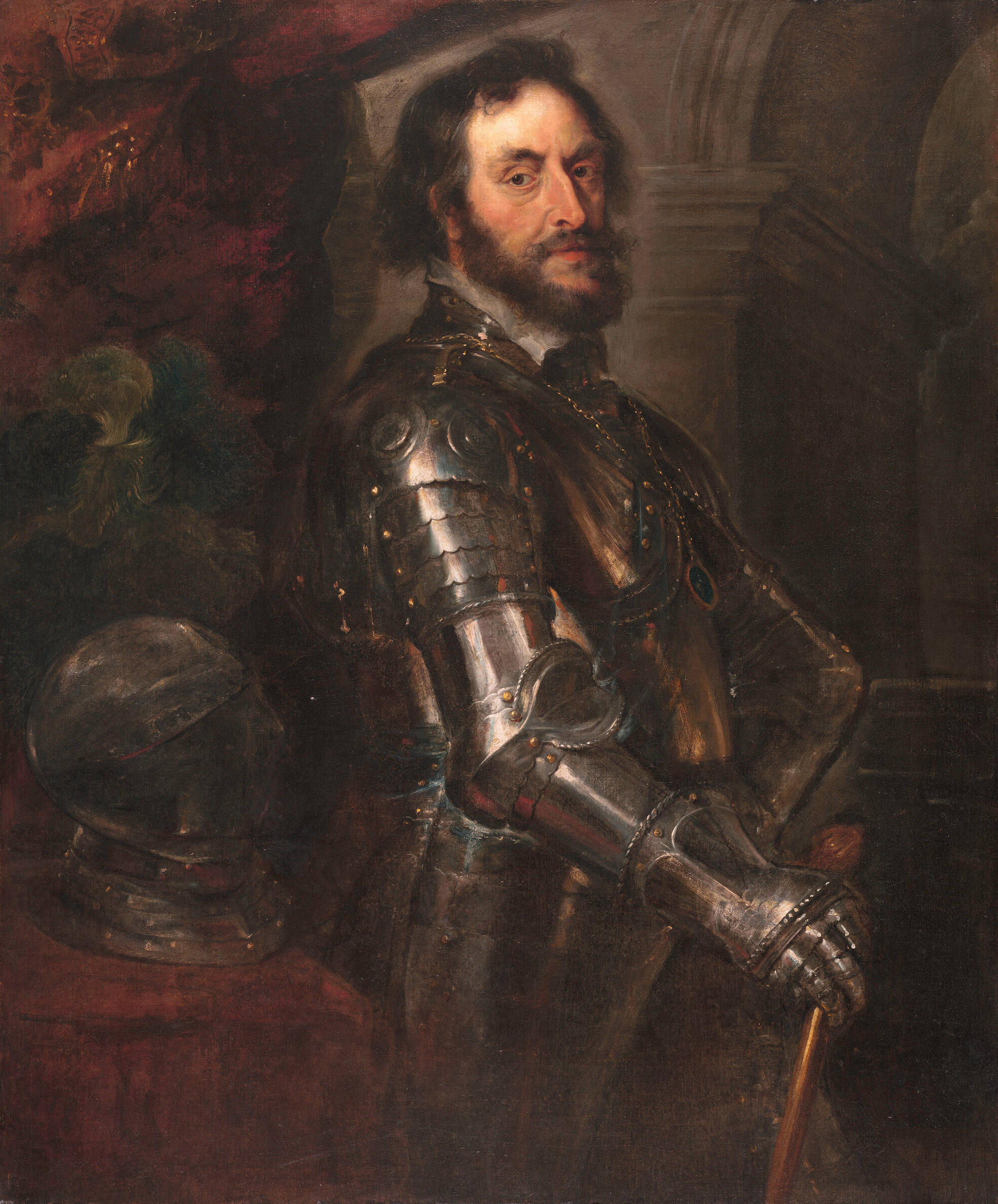A man wearing a suit of 17th-century metal armor stands before a shadowy background of stone and red velvet. 