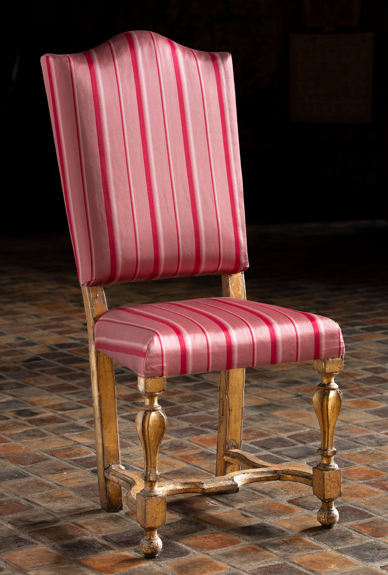 A reddish-pink upholstered side chair with vertical red stripes and gilt gold legs. 