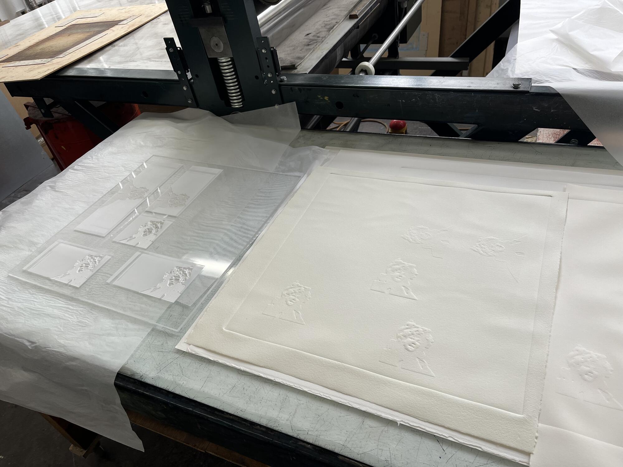 Laser engraved Plexiglas® molds with examples of paper embossments sit on a printing press in the Printmaking studio