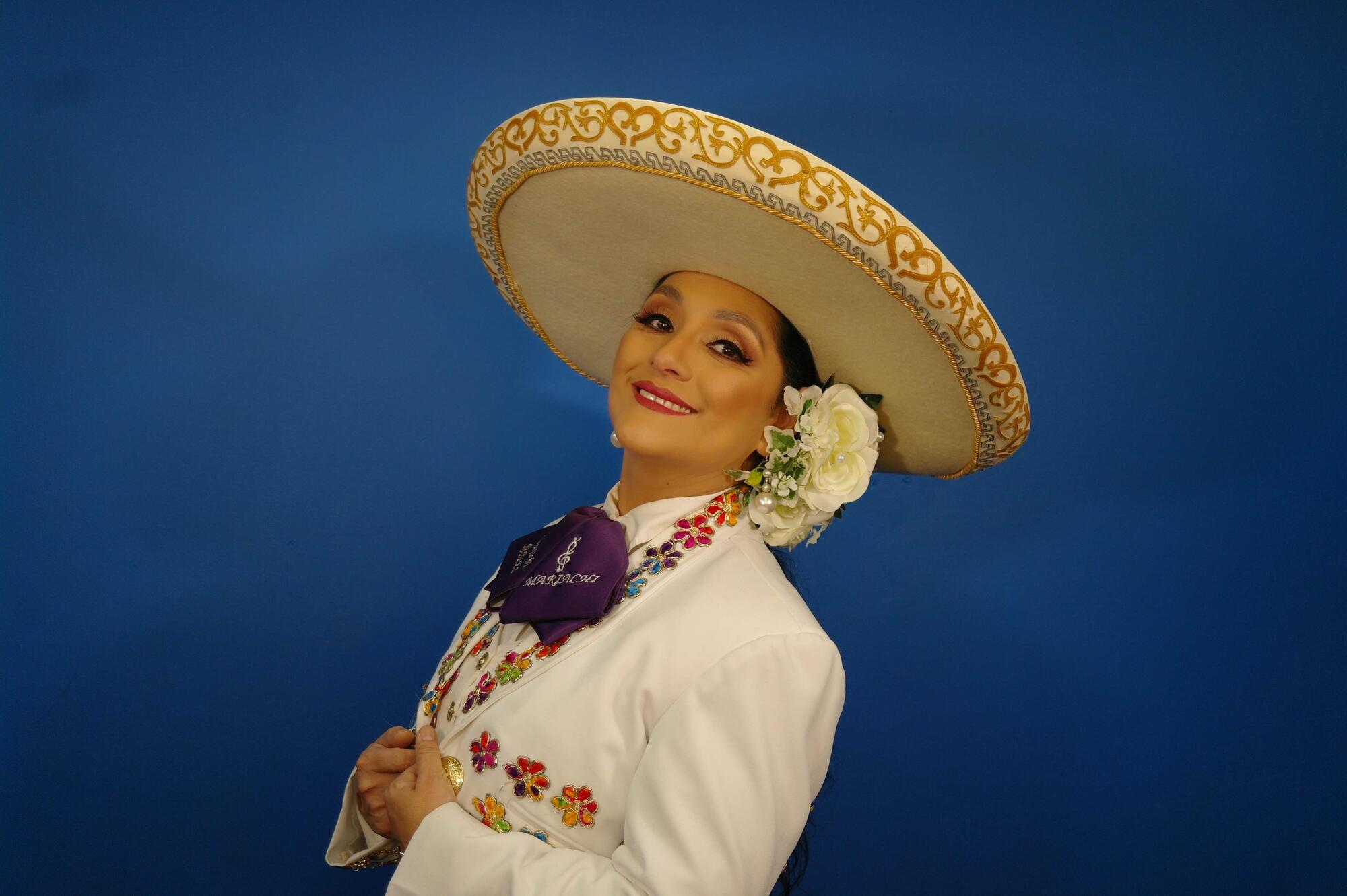 A woman wearing a sombrero decorated with gold and silver thread along the edge and a white jacket embroidered with flowers. 