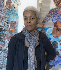 African American woman with cropped grey hair wearing a blue jacket and large floral scarf tied around her neck standing in front of of an abstract ocean scene