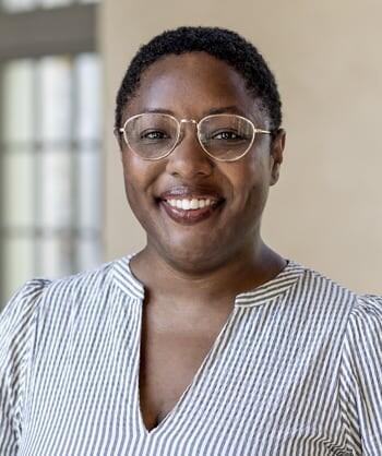 African American woman with short cropped hair wearing glasses and a v-neck top smiling at the camera. 