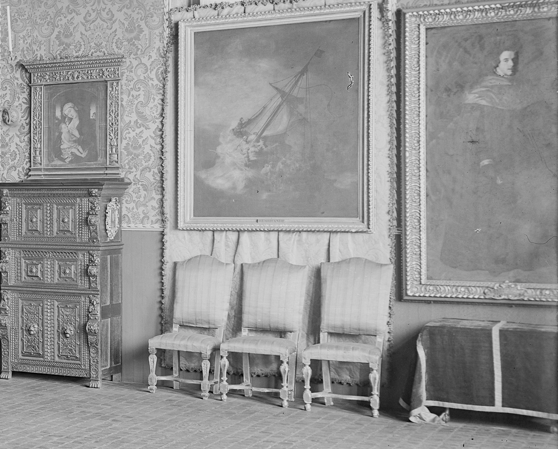 A room with European old-master paintings, sculpture, and furniture arranged eclectically. In the center of the image, three chairs with striped ombre upholstery are placed in a trio before a painted seascape. 