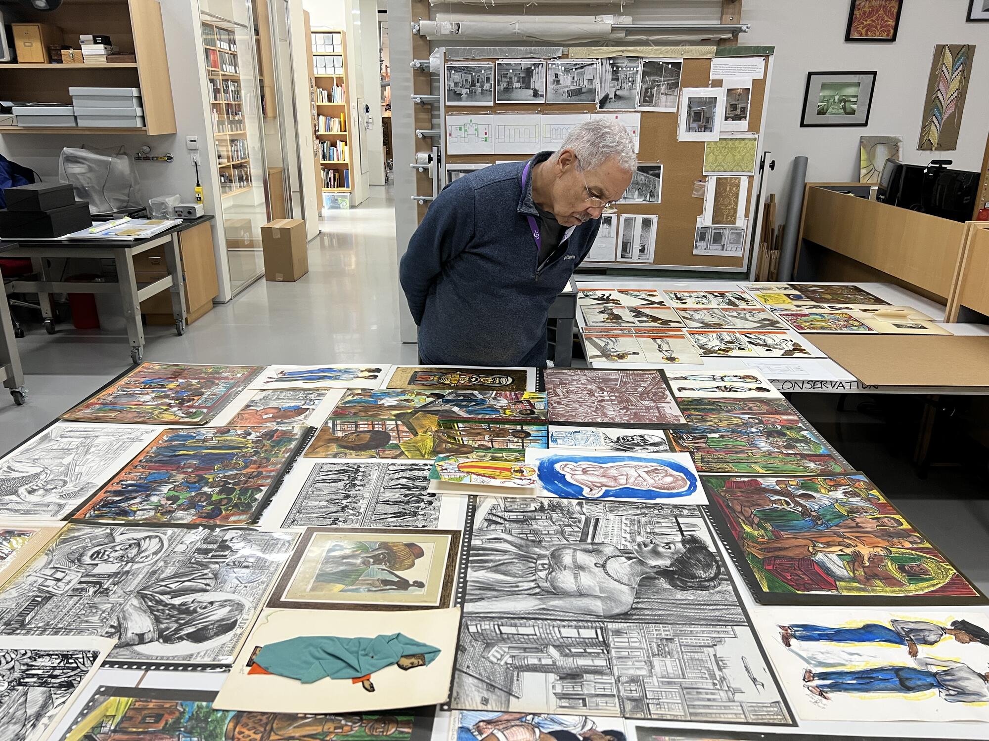 African American man with grey hair looking at a large collection of images on paper spread out over two table tops